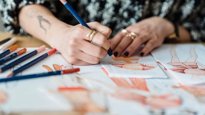 Gros plan d'une designer féminine esquissant des illustrations de mode à un bureau avec des crayons de couleur.