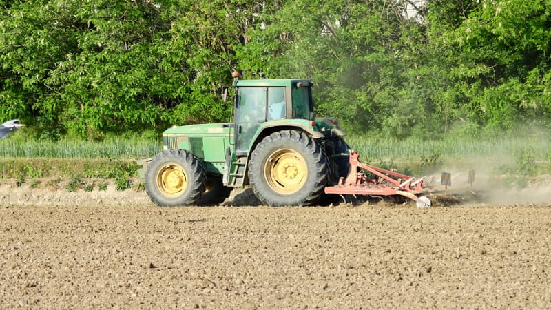 Un tracteur vert laboure un champ poussiéreux à Novara, en Italie, sous un soleil éclatant.