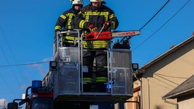 Des pompiers en action sur un camion échelle, utilisant une tronçonneuse pour des opérations de sauvetage sous un ciel bleu clair.