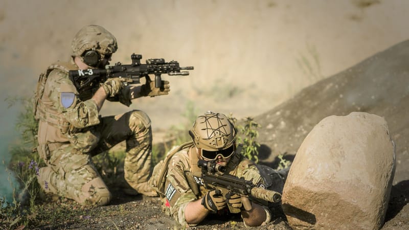 Deux soldats en uniforme de camouflage pratiquent des manœuvres tactiques dans un environnement désertique, illustrant le travail d'équipe et la précision.