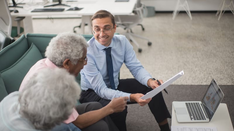 Consultant discutant des plans financiers avec des clients seniors dans un bureau moderne, utilisant des documents et un ordinateur portable.