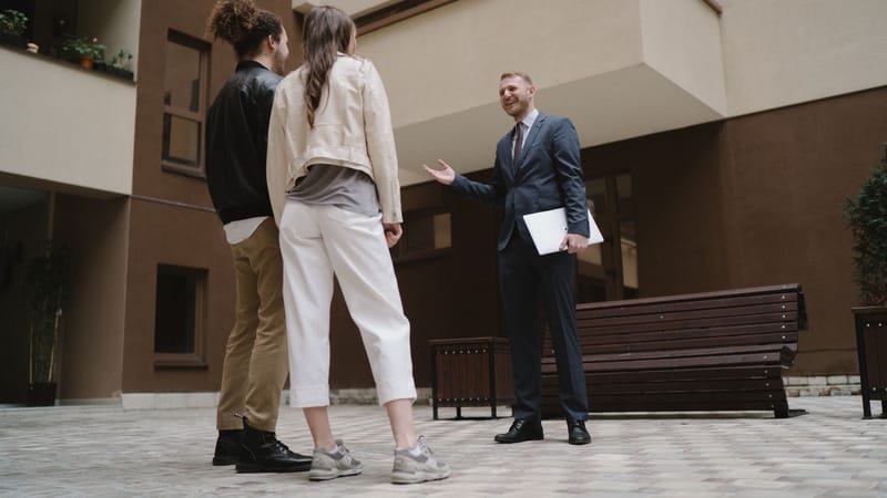 Un agent immobilier discute avec un couple dans une cour d'appartement moderne.