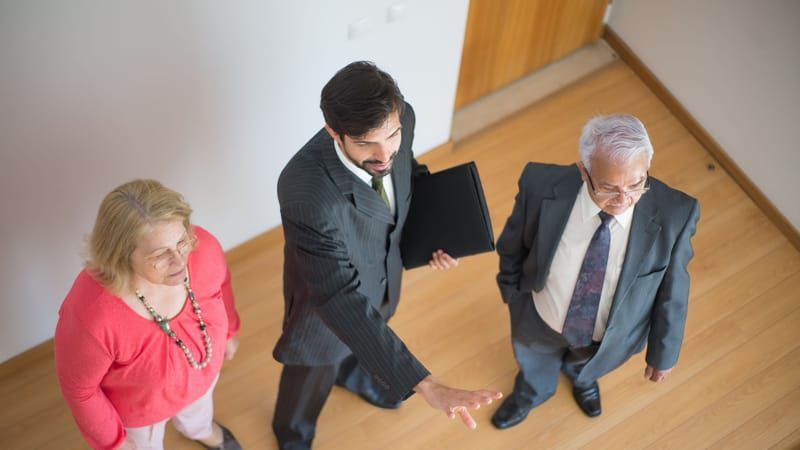 Un agent immobilier présente une propriété à un couple senior dans un cadre intérieur moderne.