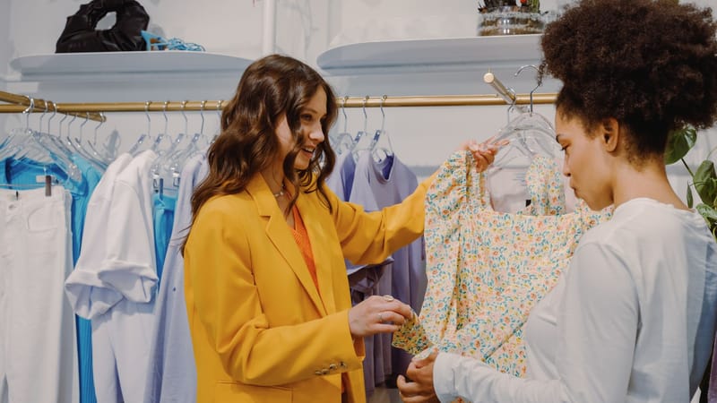 Deux femmes se rencontrent dans un magasin de vêtements tendance, discutant de choix de mode.
