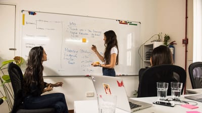 Femmes d'affaires discutant de stratégie devant un tableau blanc dans un cadre de bureau moderne.
