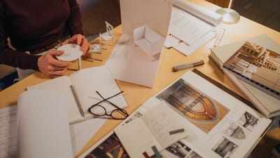 Architecte examinant un modèle miniature de design sur un bureau rempli de croquis et de plans.