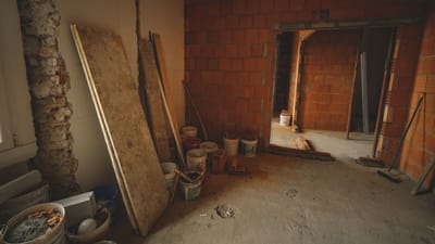 Un mur en briques rouges en construction avec des outils et des matériaux éparpillés autour dans un projet de rénovation.