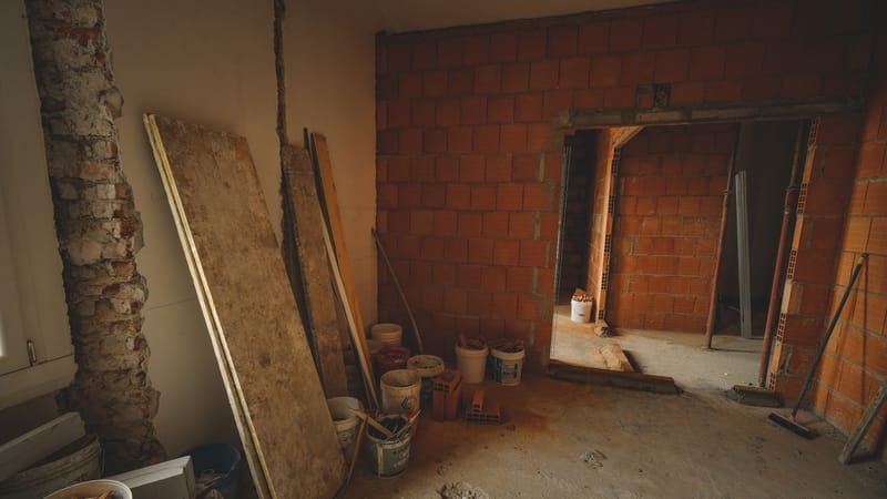 Un mur en briques rouges en construction avec des outils et des matériaux éparpillés autour dans un projet de rénovation.