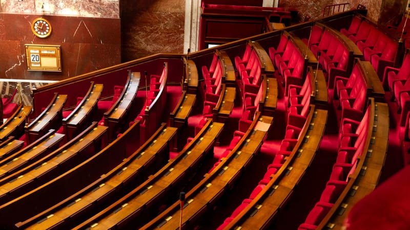 Vue intérieure luxueuse d'une salle législative avec des sièges rouges incurvés et des bureaux en bois.