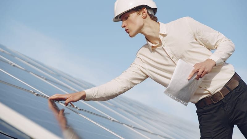 Un technicien solaire en casque inspecte des panneaux photovoltaïques sous un ciel dégagé.