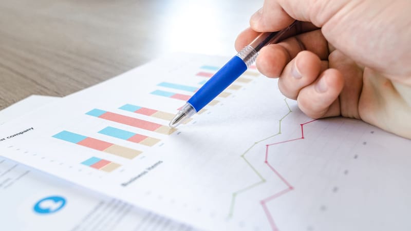 Un gros plan d'une main avec un stylo analysant des données sur des graphiques colorés à barres et en lignes sur papier.