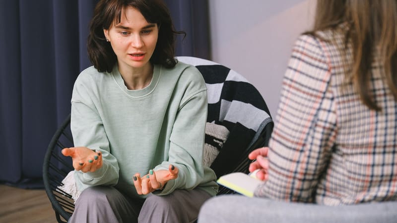 Deux femmes ayant une discussion réfléchie lors d'une séance de thérapie dans une ambiance de chambre cozy.