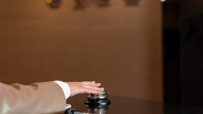 Une main pressant une cloche à la réception d'un hôtel, symbolisant le service et l'hospitalité.