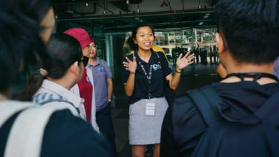 Un guide touristique guidant un groupe lors d'une visite, interagissant avec les visiteurs par gestes dans un cadre urbain extérieur.