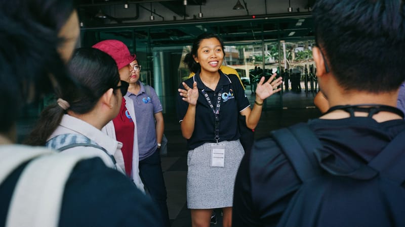 Un guide touristique guidant un groupe lors d'une visite, interagissant avec les visiteurs par gestes dans un cadre urbain extérieur.