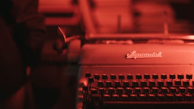 Gros plan sur une machine à écrire antique dans une pièce faiblement éclairée en rouge, évoquant une ambiance rétro.