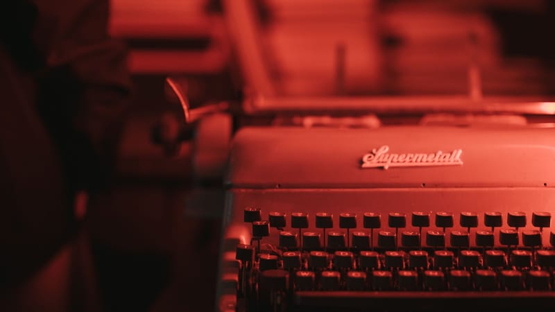 Gros plan sur une machine à écrire antique dans une pièce faiblement éclairée en rouge, évoquant une ambiance rétro.