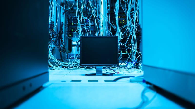 Un réseau complexe de câbles dans un centre de données avec un moniteur au premier plan.