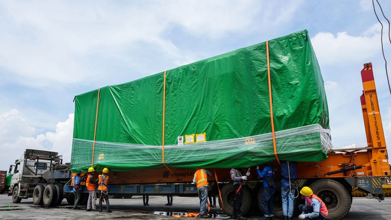 Des travailleurs manipulant un grand conteneur sur une remorque à Jakarta, mettant en avant le transport industriel.