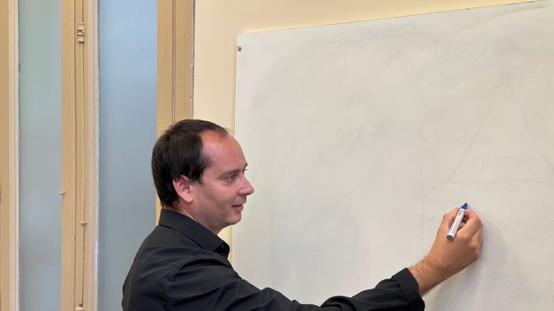 Un enseignant masculin écrivant sur un tableau blanc dans un cadre de classe.