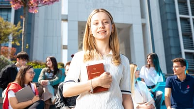 Des étudiants universitaires heureux socialisent sur le campus, avec un focus sur une jeune femme souriante tenant un livre.