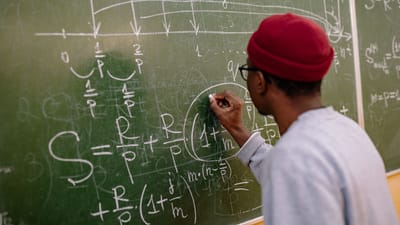 Étudiant écrivant des équations mathématiques complexes sur un tableau dans une salle de classe.