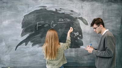 Deux étudiants discutent et résolvent une équation de physique sur le tableau.