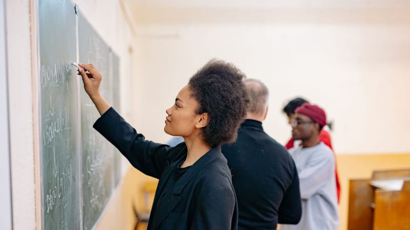 Une jeune étudiante écrivant sur un tableau noir dans une salle de classe, mettant en valeur un environnement d'apprentissage.