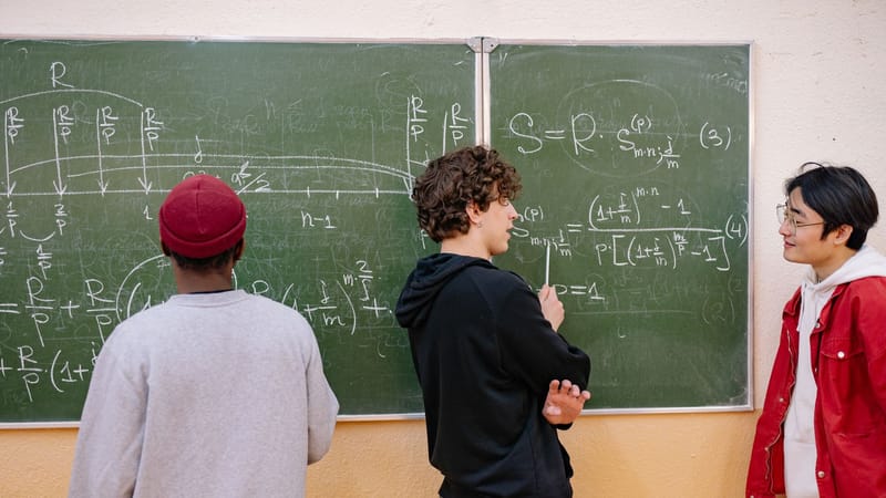 Trois étudiants discutent des équations mathématiques sur un tableau noir de classe, favorisant l'apprentissage et le travail d'équipe.