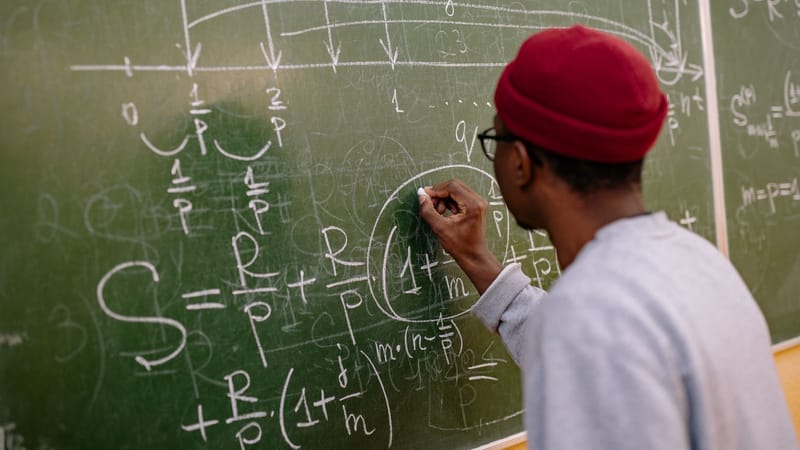 Étudiant écrivant des équations mathématiques complexes sur un tableau dans une salle de classe.