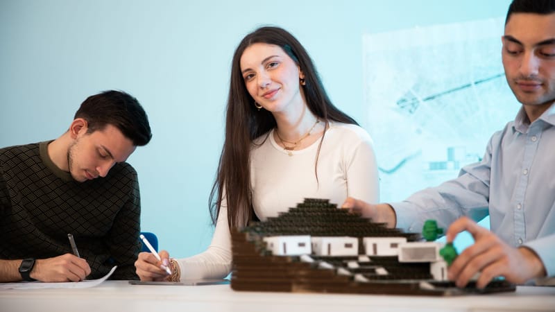 Trois personnes collaborant sur une maquette architecturale dans un environnement de bureau, mettant l'accent sur le travail d'équipe.