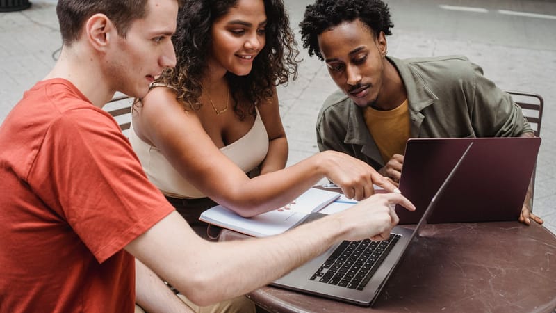 Jeune groupe multiculturel discutant d'un projet sur un ordinateur portable dans un café en plein air.