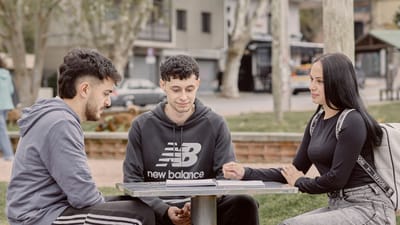 Trois jeunes adultes étudient ensemble en plein air, attablés à une table de pique-nique dans un parc uruguayen, illustrant ainsi leurs interactions sociales et leur collaboration.