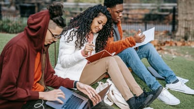 Un groupe d'étudiants divers étudie et collabore ensemble en plein air sur un campus universitaire.