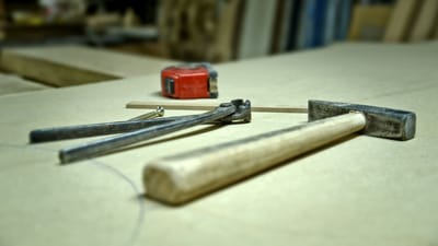 Gros plan d'un marteau, d'une vis, de pinces et d'un mètre ruban sur un établi dans un atelier.