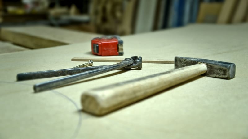 Gros plan d'un marteau, d'une vis, de pinces et d'un mètre ruban sur un établi dans un atelier.