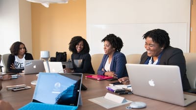 Groupe de femmes participant à une réunion collaborative autour d'une table de bureau avec des ordinateurs portables.