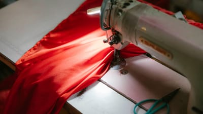 Gros plan sur une machine à coudre industrielle cousant un tissu rouge vif, éclairé sous un projecteur.