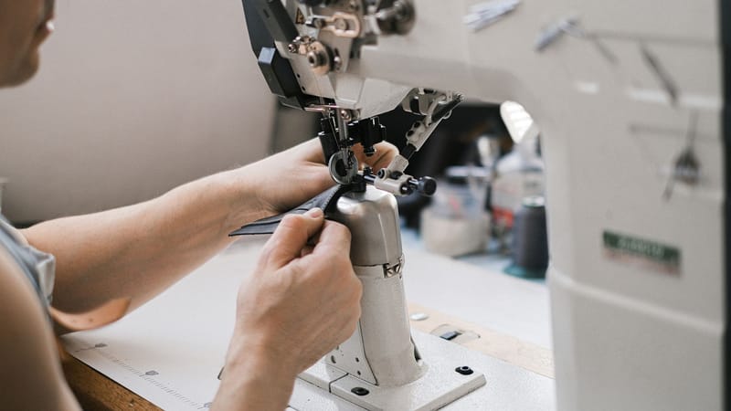 Gros plan d'un artisan du cuir au travail avec une machine à coudre industrielle.