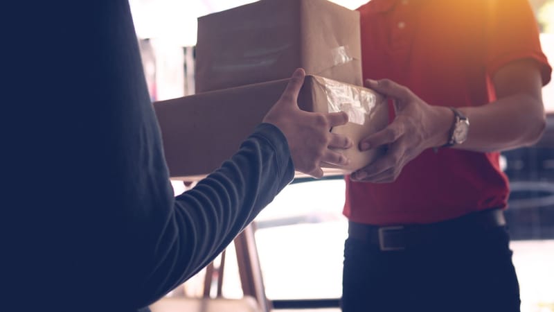 Gros plan sur un livreur remettant des colis à un client à l'intérieur.
