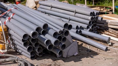 Une collection de tuyaux en PVC gris empilés soigneusement sur un chantier en extérieur.