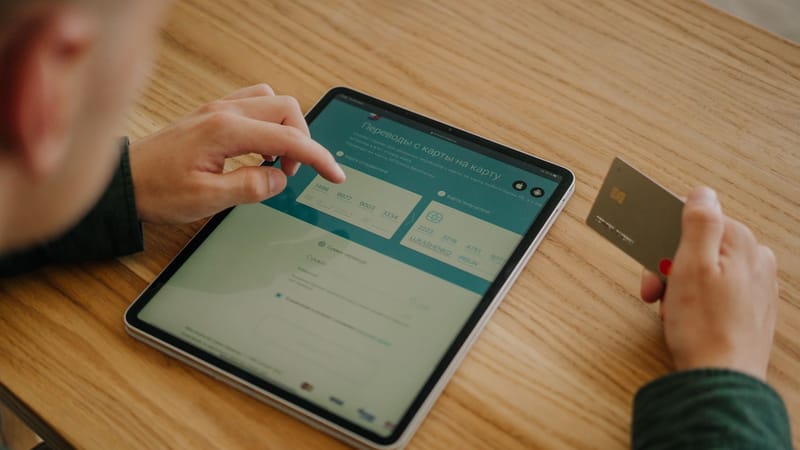 Personne effectuant un paiement en ligne à l'aide d'une tablette et d'une carte de crédit sur un bureau en bois.