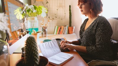 Une femme concentrée sur son travail dans son bureau à domicile avec des plantes et un ordinateur de bureau.
