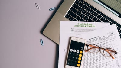 Vue de dessus des outils comptables d'une petite entreprise, y compris un formulaire fiscal, un téléphone et des lunettes sur un bureau.