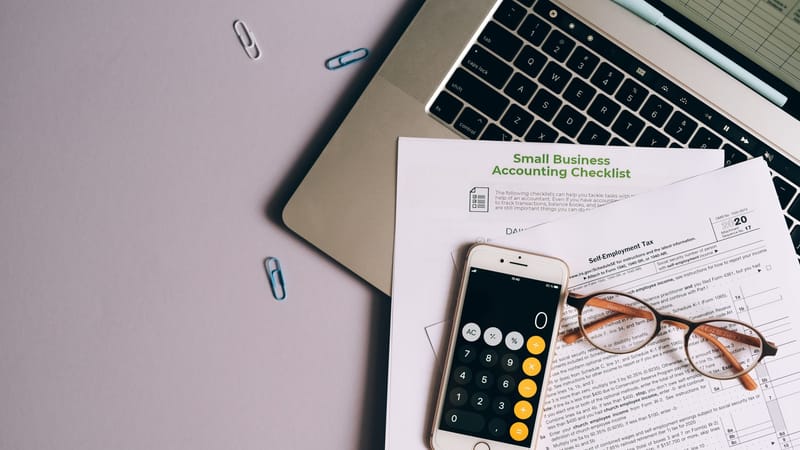 Vue de dessus des outils comptables d'une petite entreprise, y compris un formulaire fiscal, un téléphone et des lunettes sur un bureau.