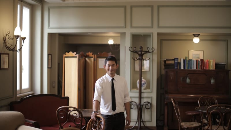 Serveur souriant se tient dans un intérieur de restaurant élégant, dégageant chaleur et professionnalisme.