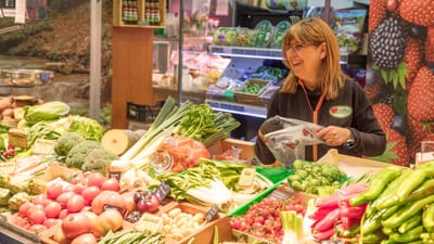Femme joyeuse vendant des produits frais dans un stand de marché animé. Idéal pour promouvoir les courses locales et une alimentation saine.