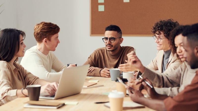 Un groupe divers de professionnels participe à une réunion collaborative autour d'une table en bois dans un environnement de bureau.