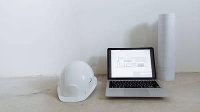 Un espace de travail propre avec un ordinateur portable, un casque de sécurité et des plans pour la planification de la construction.