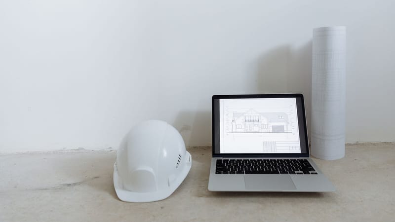 Un espace de travail propre avec un ordinateur portable, un casque de sécurité et des plans pour la planification de la construction.